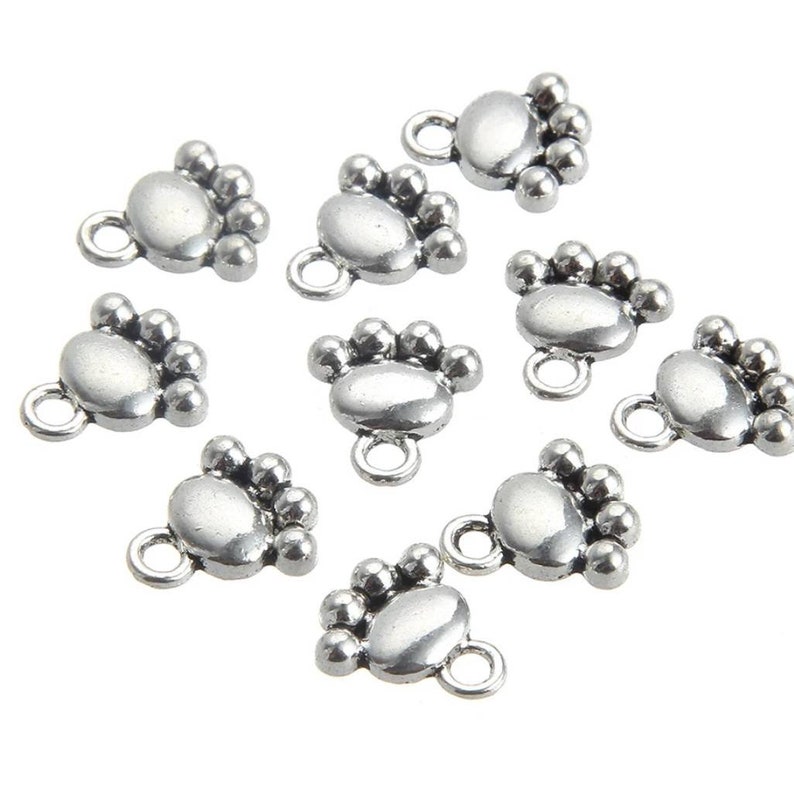 May include: Ten silver-toned metal charms shaped like a paw print with five small beads around the edge. Each charm has a loop at the top for attaching to jewelry or other crafts.