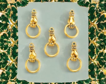 May include: Five gold-colored charms, each featuring a hand holding a ring. The charms have a detailed design on the hand and the top portion. The background is a light blue-gray color, with a decorative green and gold border.