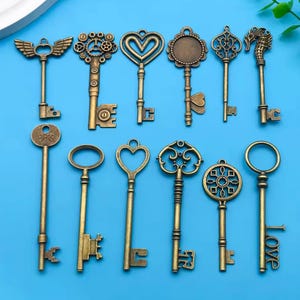 May include: A collection of antique-style keys in various designs, including wings, gears, hearts, and ornate patterns. The keys are made of a bronze-colored metal and are arranged on a blue background. Some keys have the word "LOVE" on them.