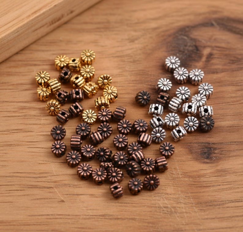 May include: A collection of small, round metal beads featuring a radial, flower-like pattern on the top and bottom surfaces. The beads are finished in three distinct metallic tones: polished gold, bright silver, and a dark, weathered copper.