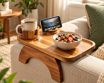 May include: A wooden sofa arm tray table featuring a built-in cup holder, a slot for a smartphone, and a flat surface area. The tray is constructed from polished wood with a natural grain, designed to rest securely over the arm of a couch.