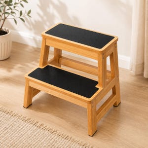 May include: A two-step stool constructed from light-toned bamboo wood. The stool features two rectangular steps, each topped with a flat, black non-slip surface. The frame is held together with visible metal screws on the side supports.