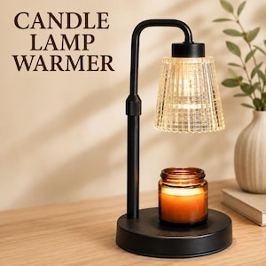 May include: A black metal candle lamp warmer with a clear, textured glass shade and a round base. The text CANDLE LAMP WARMER is printed in dark brown. A small amber glass jar candle sits on the base, illuminated by the warm light from above.
