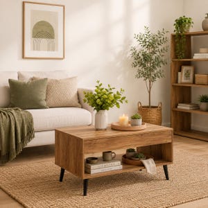 May include: A rectangular wooden coffee table with a top surface, a lower storage shelf, and four black tapered legs. The table holds a white ribbed vase with green foliage, a wooden tray with a candle, and books on the lower shelf.