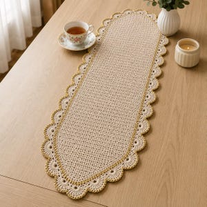 Puede incluir: Un camino de mesa ovalado de ganchillo en color beige con un patrón de puntos denso en el centro y un borde festoneado decorativo delineado con hilo amarillo dorado, creando una pieza textil texturizada y detallada para mesas.