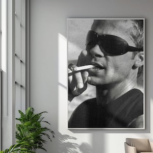 May include: A large, rectangular, black and white wall art print featuring a close-up portrait of a person wearing dark, wrap-around sunglasses. The person is holding a lit cigarette to their lips, captured in a high-contrast, grainy photographic style.