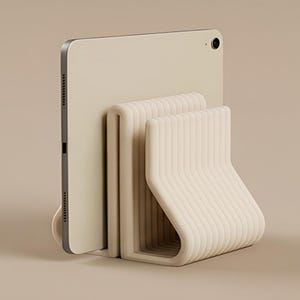 May include: A light beige tablet stand featuring a series of parallel, curved, ribbed vertical supports that hold a flat, rectangular tablet device in an upright position. The stand has a smooth, matte finish and a consistent, uniform colour.