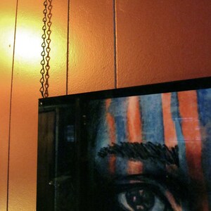 May include: A close-up of a painting of a person's eye with blue and orange stripes. The eye is looking directly at the viewer.