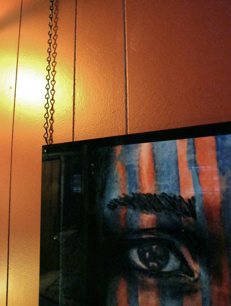 May include: A close-up of a painting of a person's eye with blue and orange stripes. The eye is looking directly at the viewer.