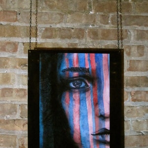 May include: A framed watercolor painting of a person's face with blue and pink stripes painted across the face. The background is black.