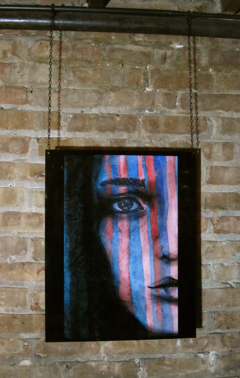 May include: A framed watercolor painting of a person's face with blue and pink stripes painted across the face. The background is black.