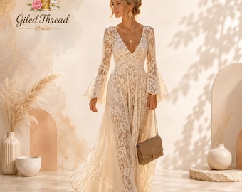 May include: A floor-length cream-colored lace dress featuring long bell sleeves, a deep V-neckline, and a fitted bodice. The dress is crafted from intricate floral lace fabric and is paired with a structured beige rectangular shoulder bag.
