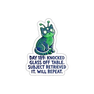 May include: A die-cut sticker featuring a three-eyed cat with antennae, rendered in blue and green line art. Below the cat, the text reads: DAY 189: KNOCKED GLASS OFF TABLE. SUBJECT RETRIEVED IT. WILL REPEAT. The design has a white border.