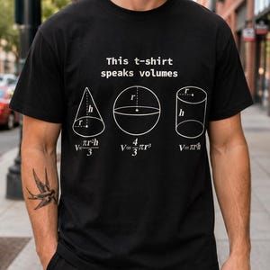 Puede incluir: Una camiseta negra de manga corta con el texto blanco "This t-shirt speaks volumes" sobre ilustraciones de un cono, una esfera y un cilindro, con sus respectivas fórmulas de volumen geométrico impresas en blanco debajo de cada forma.