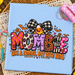 May include: A light blue folder featuring a graphic design with the text "MOMBEE LIKE A ZOMBIE, BUT WITH KIDS". The design includes a candy corn character with a black and white plaid bow, orange bats, flowers, and colorful patterned letters.