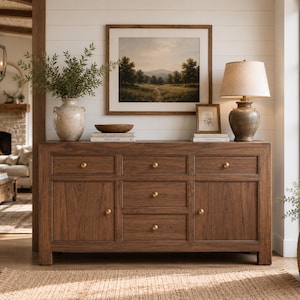 Könnte beinhalten: Ein rechteckiges Sideboard aus Holz mit drei oberen Schubladen, zwei unteren Schubladen in der Mitte und zwei Seitenschränken. Jede Schublade und Schranktür ist mit einem kleinen, runden, goldfarbenen Knopf versehen. Das Holz hat eine sichtbare Maserung.