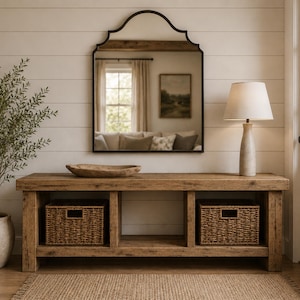 May include: A rectangular wooden console table with a natural finish, featuring three open storage compartments, two woven wicker baskets, a wooden bowl, and a table lamp with a white shade, positioned below a large arched wall mirror.
