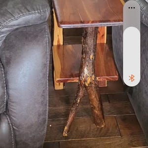 May include: A two-tiered side table constructed from polished wood with a rectangular top and a lower shelf. The table features a central support leg made from a thick, textured tree branch with visible bark, providing a natural aesthetic.
