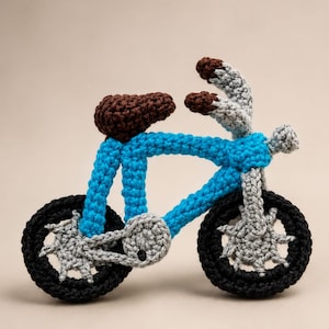 Puede incluir: Una bicicleta de ganchillo con marco azul, ruedas negras, asiento marrón y manillar y engranajes grises. El texto superior dice Mini Crochet Bicycle Amigurumi Pattern. El número 1 es visible en la esquina inferior derecha de la imagen.