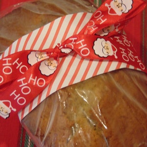 May include: A loaf of bread wrapped in clear plastic and tied with a red and white striped ribbon. The ribbon has a repeating pattern of "HO HO" and a cartoon image of Santa Claus.