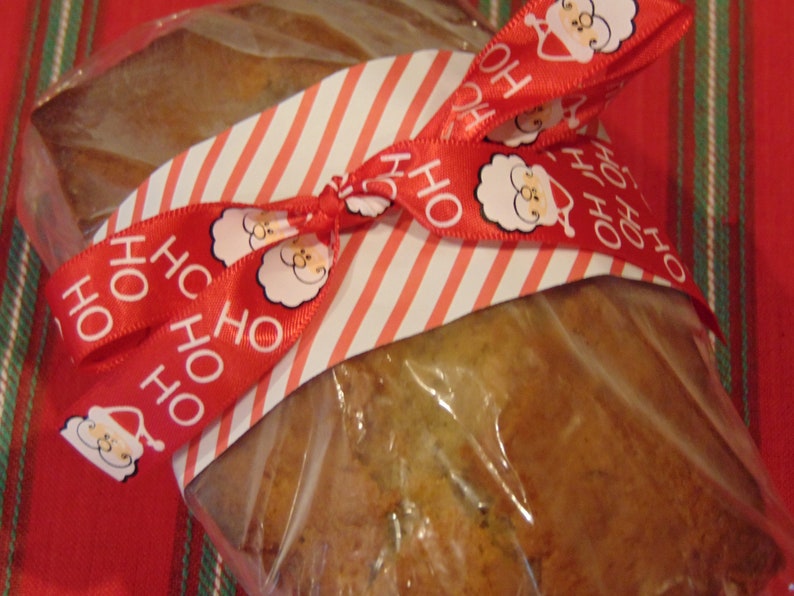 May include: A loaf of bread wrapped in clear plastic and tied with a red and white striped ribbon. The ribbon has a repeating pattern of "HO HO" and a cartoon image of Santa Claus.