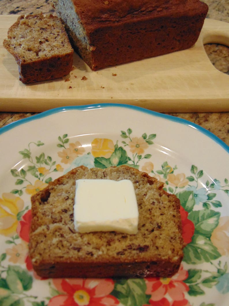 May include: A slice of banana bread with a pat of butter on top, on a white plate with a floral pattern.
