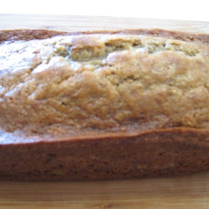 May include: A loaf of freshly baked banana bread, golden brown and slightly glossy, sitting on a wooden cutting board.