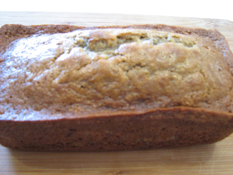 May include: A loaf of freshly baked banana bread, golden brown and slightly glossy, sitting on a wooden cutting board.