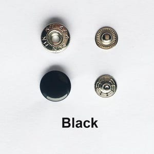 May include: A set of four metal and black plastic snap fasteners. The top left piece is a silver-toned metal cap with the text SUN HK 484. The bottom left is a smooth black circular cap. The right side shows two silver-toned metal back components.
