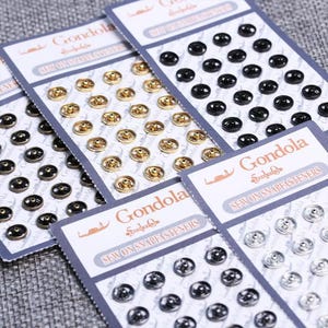 May include: Multiple retail cards of Gondola brand sew-on snap fasteners in various metallic finishes including gold, silver, and black. Each card features rows of circular metal snaps with a central stud and a raised rim, designed for garment closure.
