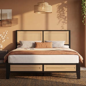 May include: A bed frame featuring a black metal structure with natural light-colored woven cane panels on the headboard and footboard. The bed is dressed with a white mattress, a solid tan blanket, and two patterned pillows in shades of gray and white.