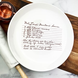 May include: White ceramic plate with a handwritten recipe for Mel Lardi Mustard Sauce. The recipe includes ingredients like Coleman's mustard, coffee, cream, oil, and salt. The instructions include stirring, adding cider vinegar, and beating egg yolks.
