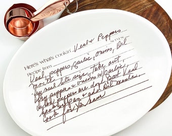 May include: White oval serving platter with a handwritten recipe for veal peppers, garlic, onions, and del. The recipe is written in brown ink on a white background with black lines.