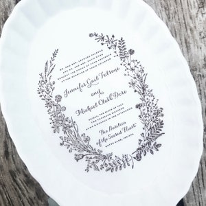May include: A white paper plate with a black and white floral wreath design. The text inside the wreath reads "MR. AND MRS. LEONARD FALSONE AND DR. AND MRS. DAVID DORE REQUEST THE HONOR OF YOUR PRESENCE AT THE MARRIAGE OF THEIR CHILDREN Jennifer Gail Falsone and Michael Clark Dore FRIDAY, THE SIXTH OF JULY TWO THOUSAND EIGHTEEN AT TWO O'CLOCK IN THE AFTERNOON The Basilica of the Sacred Heart NOTRE DAME, INDIANA"
