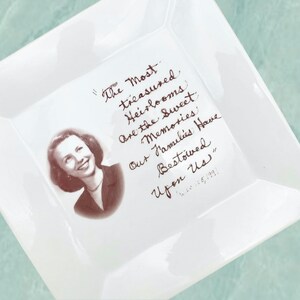 May include: A white square ceramic dish with a handwritten quote in brown ink. The quote reads: "The Most treasured Heirlooms are the sweet Memories Our Families Have Bestowed Upon Us." A black and white photo of a woman is in the center of the dish.