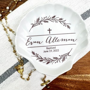 May include: White ceramic seashell dish with a brown floral design and the text "Evan Alleman Baptized June 19, 2022".
