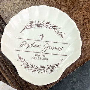 May include: White ceramic seashell dish with a brown floral design and the text "Stephen James Baptized April 28 2024".
