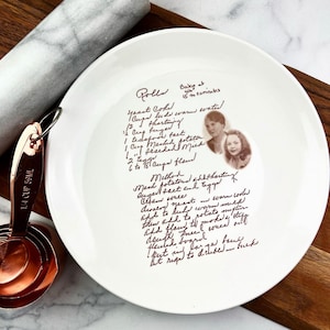 May include: White ceramic plate with a handwritten recipe for rolls, including ingredients and instructions. The plate features a sepia-toned photo of two women. Copper measuring cups and a marble rolling pin are in the background.
