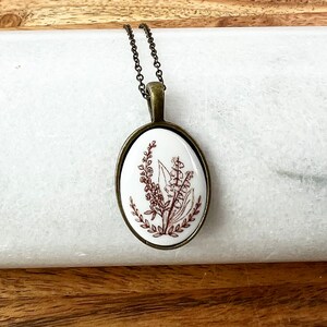 May include: A white oval pendant necklace with a brown floral design. The pendant is on a brown chain.