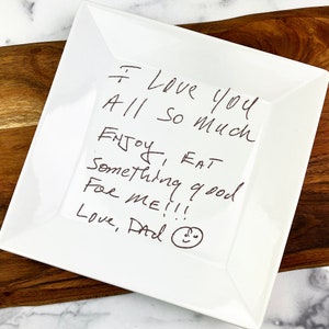 May include: White square ceramic plate with a handwritten message that says "I Love you All so much ENJOY, EAT Something good FOR ME!!! Love, Dad" and a simple smiley face.