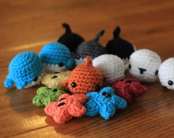 May include: A collection of small, handmade crochet plushies featuring various sea creatures including sharks and starfish in vibrant colors like blue, orange, white, black, green, and red, each with small black bead eyes.