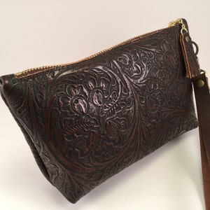 May include: A brown leather clutch with a floral embossed design and a matching brown leather strap.