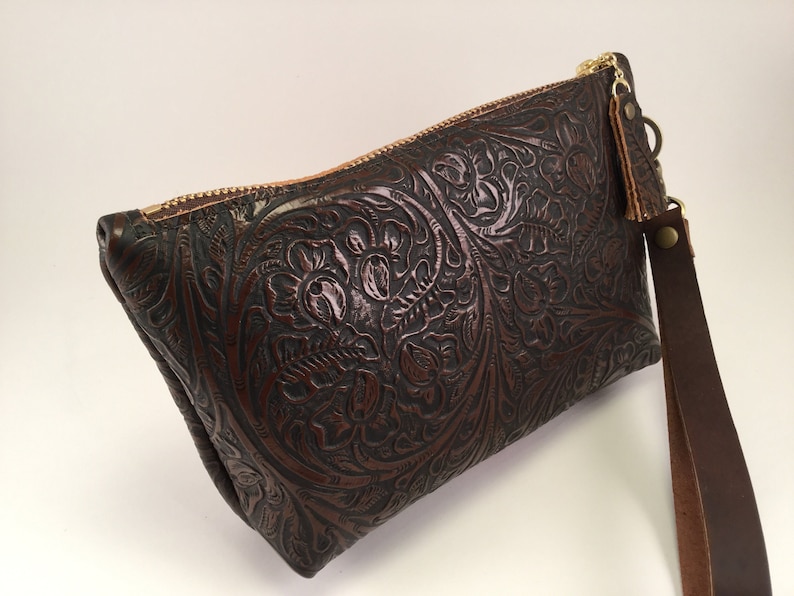 May include: A brown leather clutch with a floral embossed design and a matching brown leather strap.