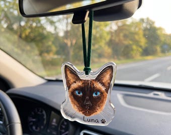 Pode incluir: Um ornamento de carro em acrílico transparente em forma de cabeça de gato com o retrato de um gato siamês castanho de olhos azul-brilhante. O nome Luna está impresso a preto sob a cara do gato, seguido de um pequeno ícone de pata preta.