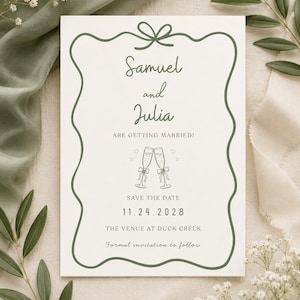 May include: A white rectangular save the date card with a dark green wavy border and a bow at the top. The text reads Samuel and Julia ARE GETTING MARRIED! with a champagne glass illustration, the date 11.24.2028, and THE VENUE AT DUCK CREEK.