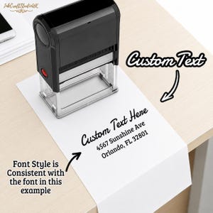 Può includere: Un timbro autoinchiostrante nero posizionato su un foglio di carta bianco. La carta mostra il testo stampato Custom Text Here, 4567 Sunshine Ave, Orlando, FL 32801. Il timbro presenta un corpo nero rettangolare con una base trasparente.