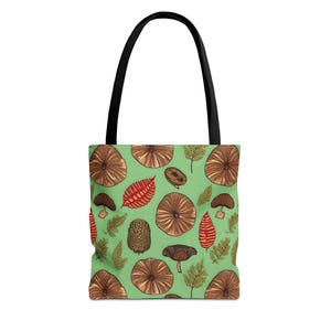 May include: A tote bag with black handles featuring a light green background patterned with brown mushroom caps, orange-red leaves, and green fern fronds. The illustrations are rendered in a detailed line art style across the entire surface.