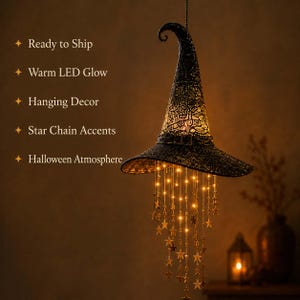 May include: A black lace witch hat hanging decoration featuring a warm LED glow. The hat is adorned with a buckle and suspended from it are multiple delicate chains decorated with small gold-colored stars that illuminate with a soft light.
