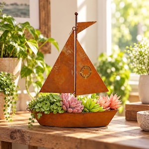 May include: A decorative metal sailboat planter with a rusted orange finish, featuring a mast and triangular sails. The boat hull is filled with a variety of green and pink succulent plants, including a trailing vine and rosette-shaped succulents.