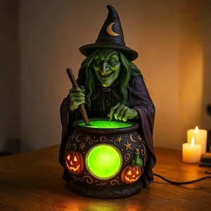 May include: A witch figurine wearing a dark pointed hat with a crescent moon emblem, featuring green skin and long hair. The witch stirs a black cauldron decorated with stars, moons, and two jack-o'-lanterns, which glows with a bright green light.